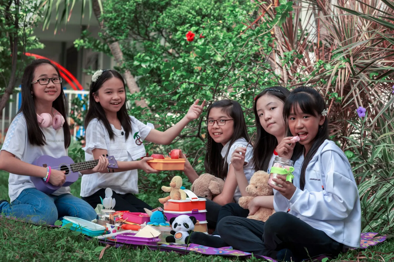 Group of children having a picnic outdoors with toys and snacks, enjoying friendship and nature.