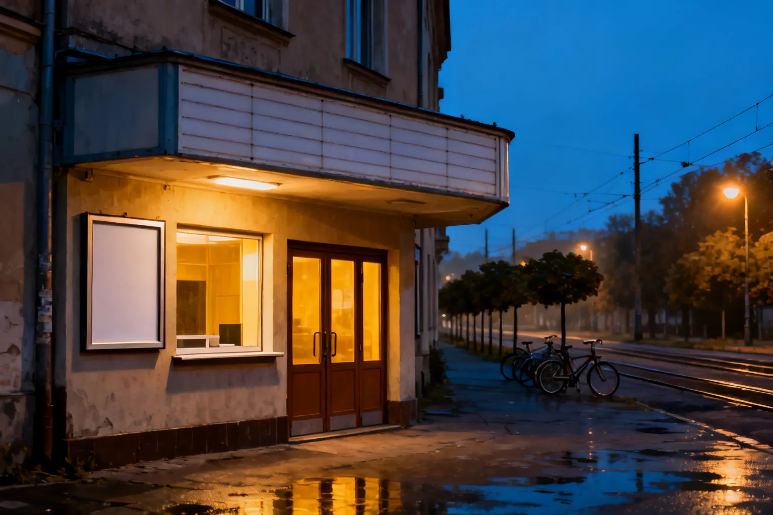 Przytulne, zamknięte kino studyjne o ciepłym wnętrzu widocznym przez szyby, wieczorna ulica Katowic z lampami i mokrym chodnikiem.