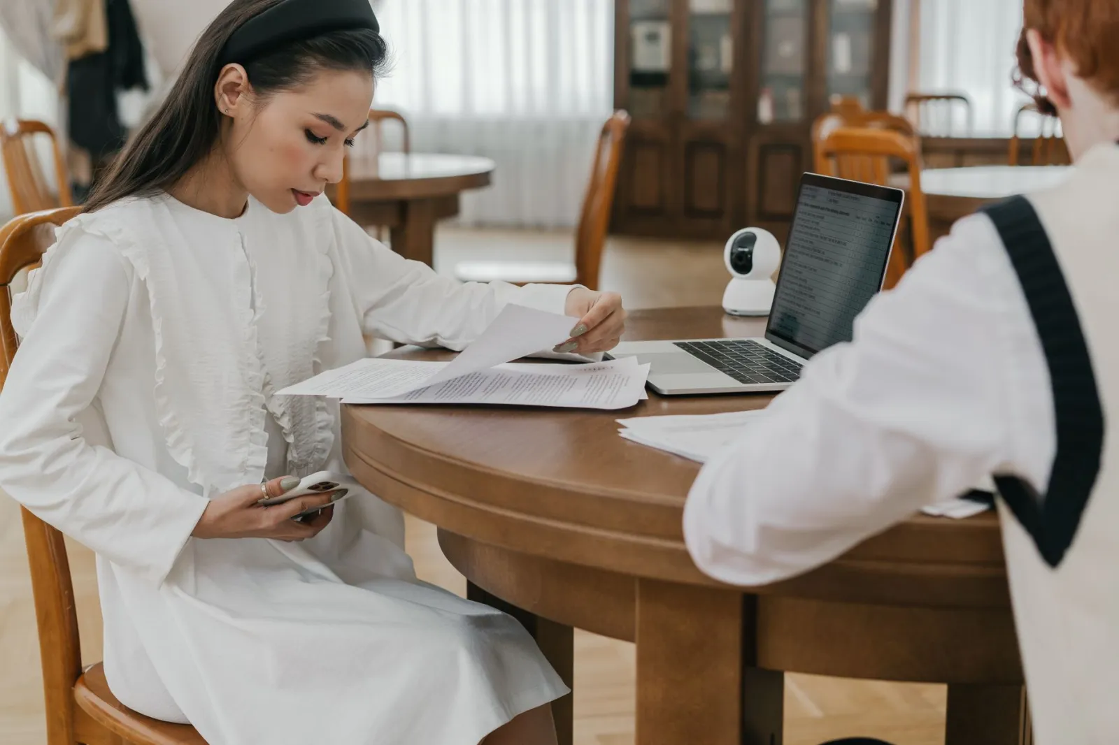 Two students focusing on their studies at a communal table, using laptops and documents.