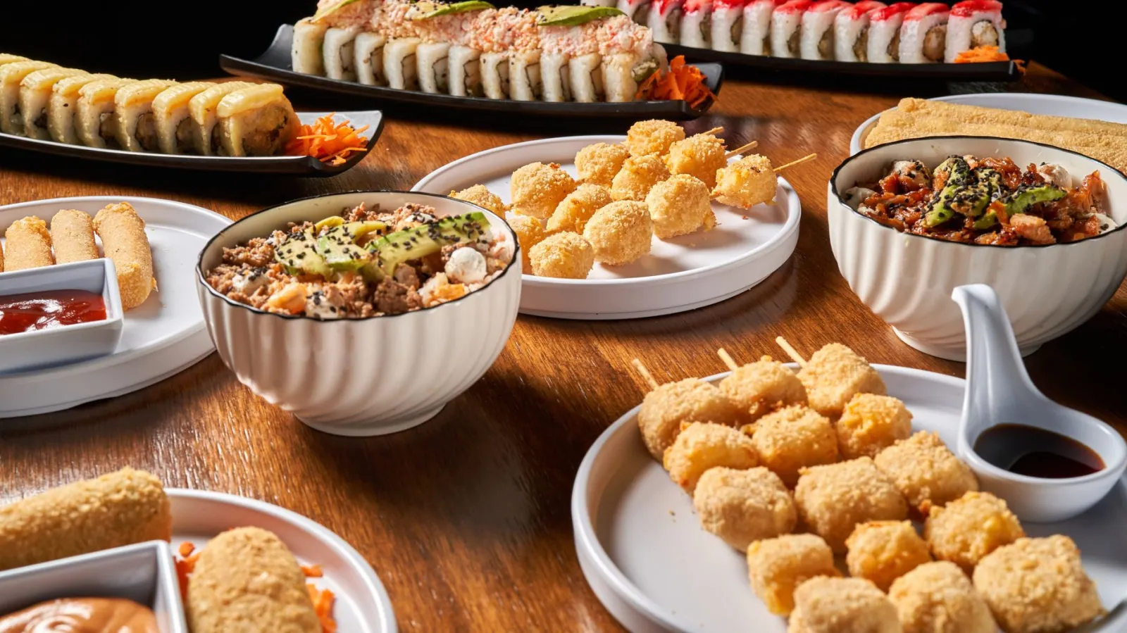 A variety of Asian dishes including sushi, skewers, and rice bowls on a wooden table.