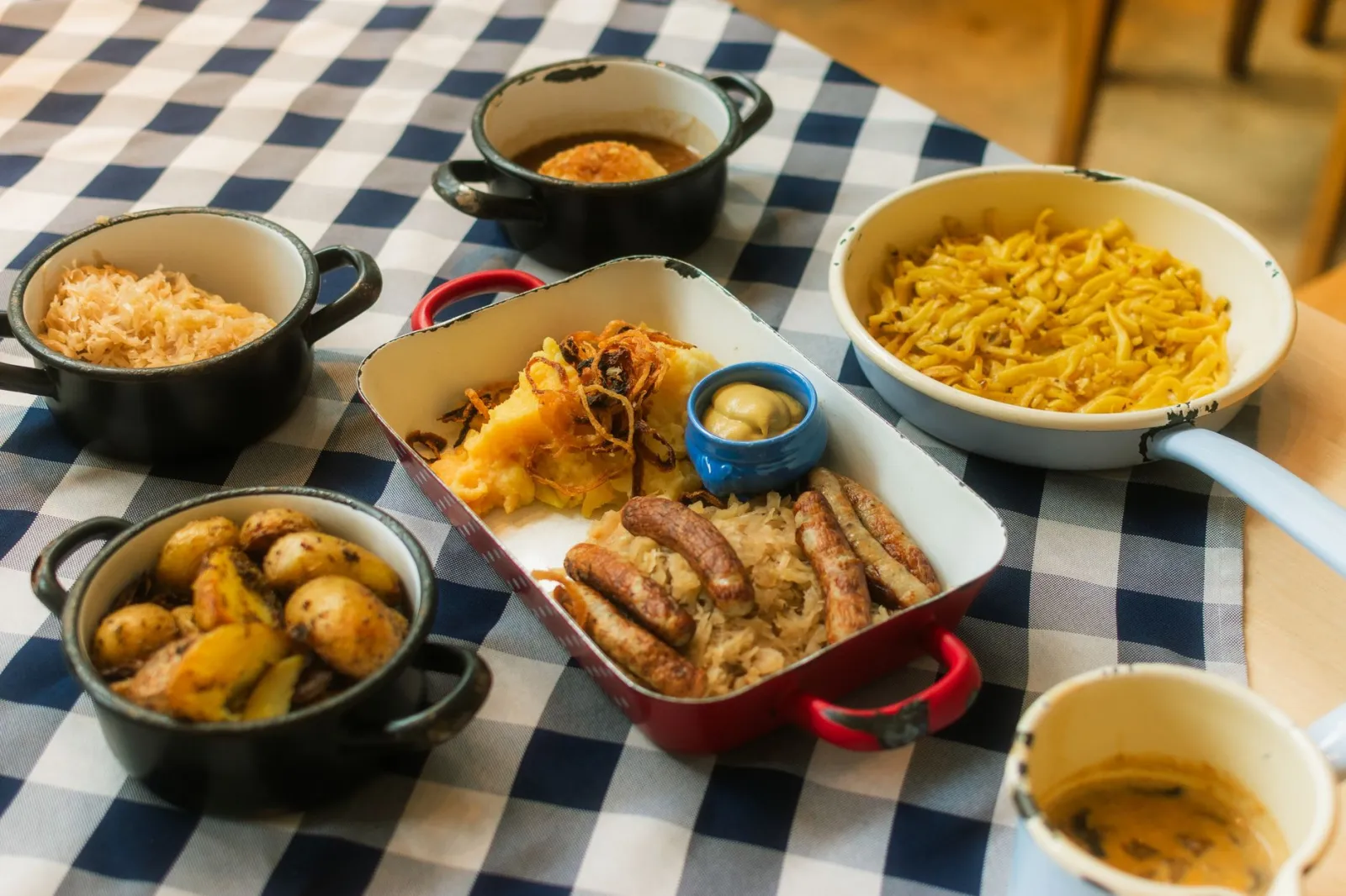 A delicious assortment of German cuisine featuring sausages, potatoes, sauerkraut, and more on a checkered tablecloth.
